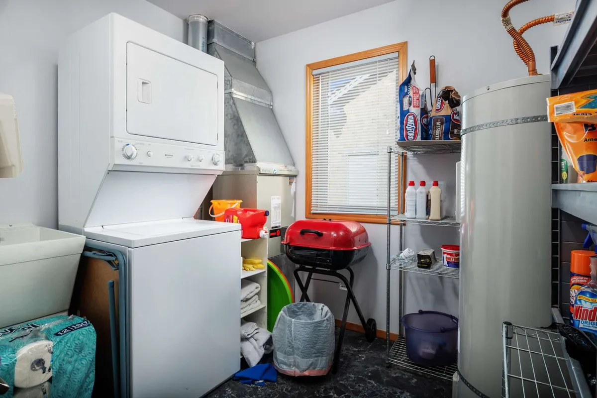 This image features a laundry area with a window letting in natural light, a washing machine and dryer, and a glimpse of a grill. The presence of the window subtly hints at a connection to the outdoors, while the grill suggests opportunities for backyard gatherings and outdoor activity.