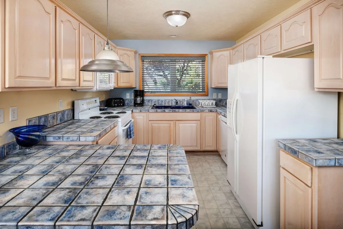 The kitchen features a substantial island, stainless steel appliances, and distinctive blue tiled countertops with light wood cabinetry. The layout is designed for effortless meal preparation and group cooking, making it perfect for preparing fresh-caught fish or family favorites.