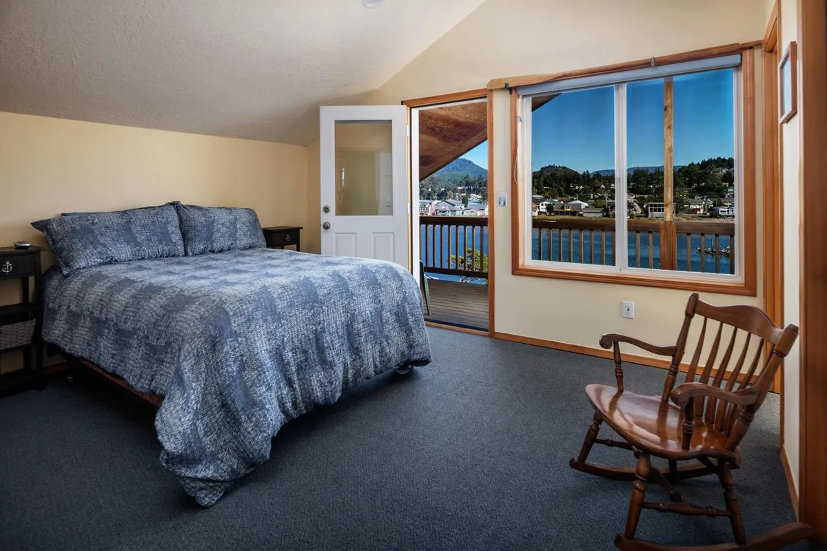 A serene bedroom scene with a comfortable bed positioned near a large window, a rocking chair by the window, and a tranquil view beyond. The natural light fills the space, evoking peaceful mornings or relaxing afternoons. The window suggests a scenic outlook, possibly the river mentioned in the section.
