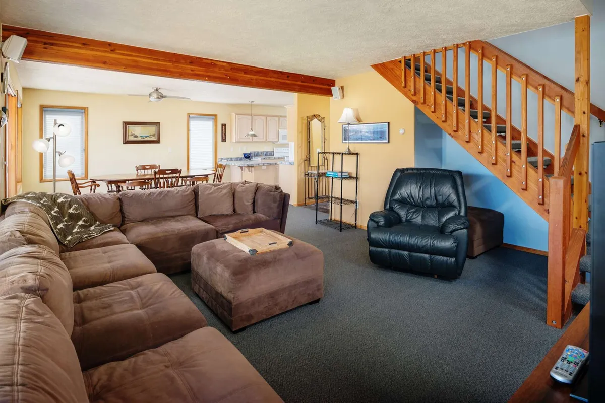 The scene shows a spacious living area with a large sectional couch, a coffee table, a staircase, and a dining area in view. The open-concept design suggests a welcoming environment for family and pets to gather before or after coastal adventures.