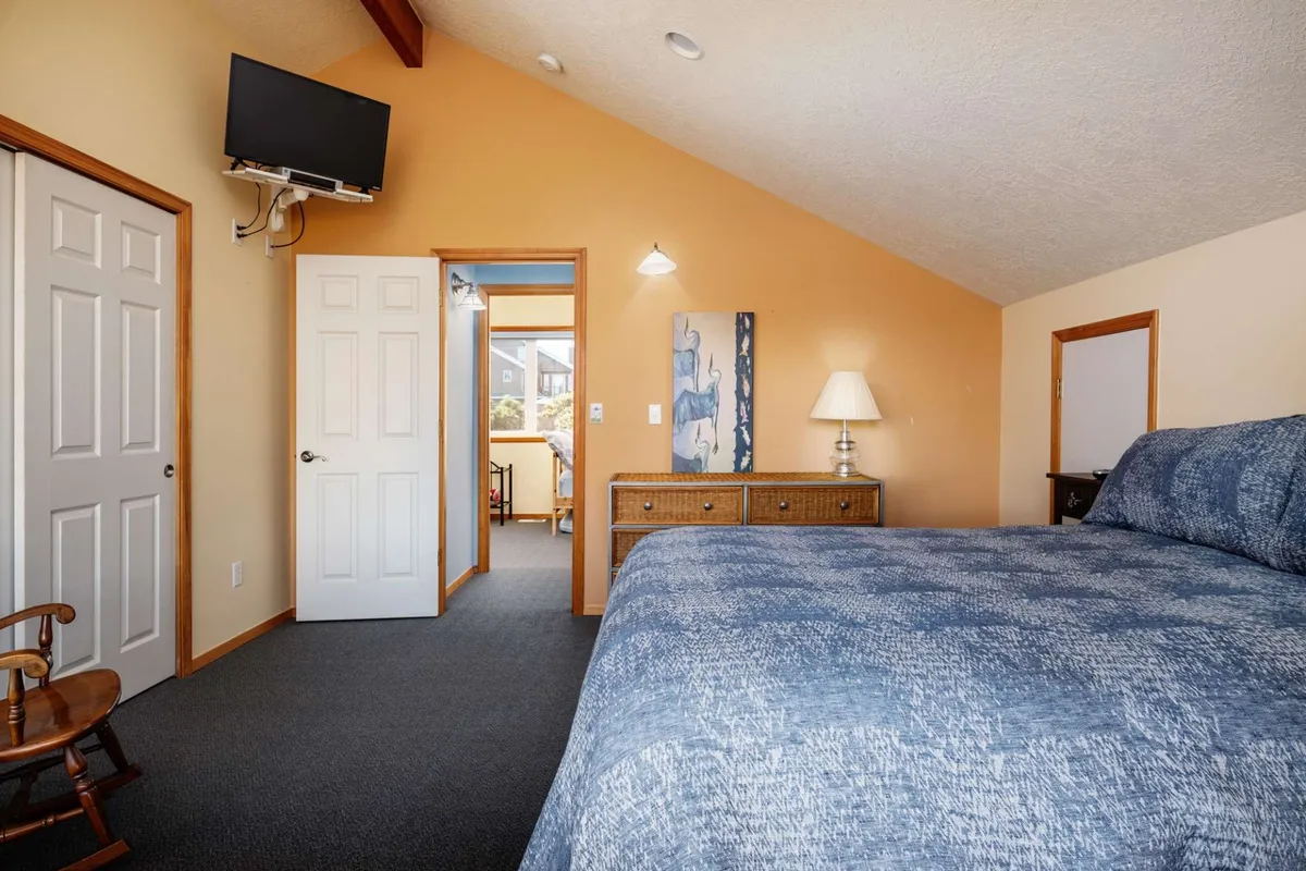 A cozy bedroom with a large bed, chest of drawers, and a door leading out, bathed in comfortable light. The arrangement suggests a space welcoming to relaxation and rest, ideal for guests or family members.