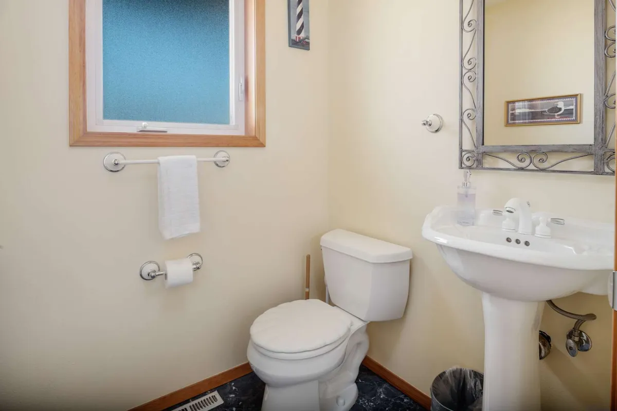 A compact, practical half bathroom is shown with a toilet, sink, mirror, and a small window that lets in natural light. The clean, uncluttered space is easily accessible for guests’ comfort.