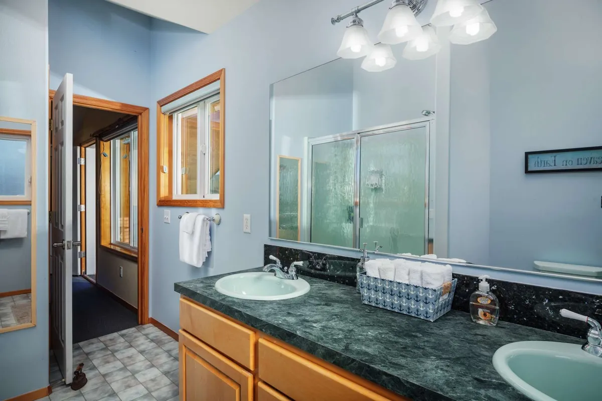 A bright, contemporary bathroom with dual sinks, a large mirror, and a spacious glass shower enclosure. Natural light streams through windows, highlighting the calming and clean design ideal for morning or evening routines.